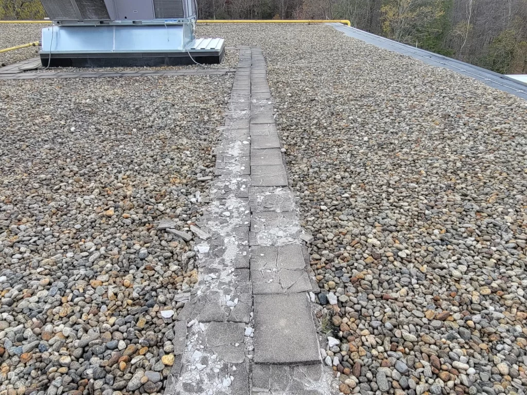 Deteriorated walkpads on a flat gravel-covered roof next to an HVAC unit.