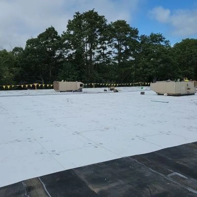 A commercial flat roof mid-renovation, with white roofing membrane being installed and equipment on-site.
