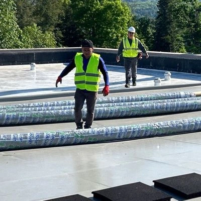 Roofing contractors in safety gear laying out rolled roofing membrane materials on a commercial flat roof surface